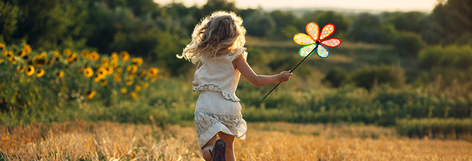 young girl running in a field holding a colorful flower toy sunshine and nature six enjoyment