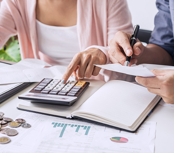 two people calculating finances using a calculator and analyzing documents with charts and coins on a table