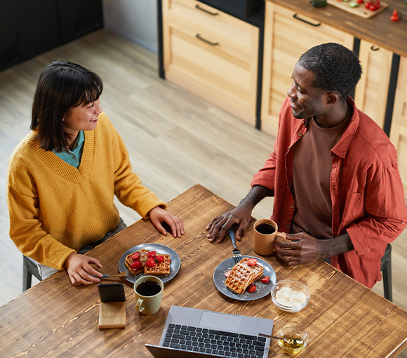 man and woman enjoying breakfast together with waffles and fruits coffee and laptop on table atmosphere for two