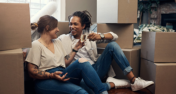 a joyful couple toasting with drinks sitting among moving boxes celebrating their new home and experiences